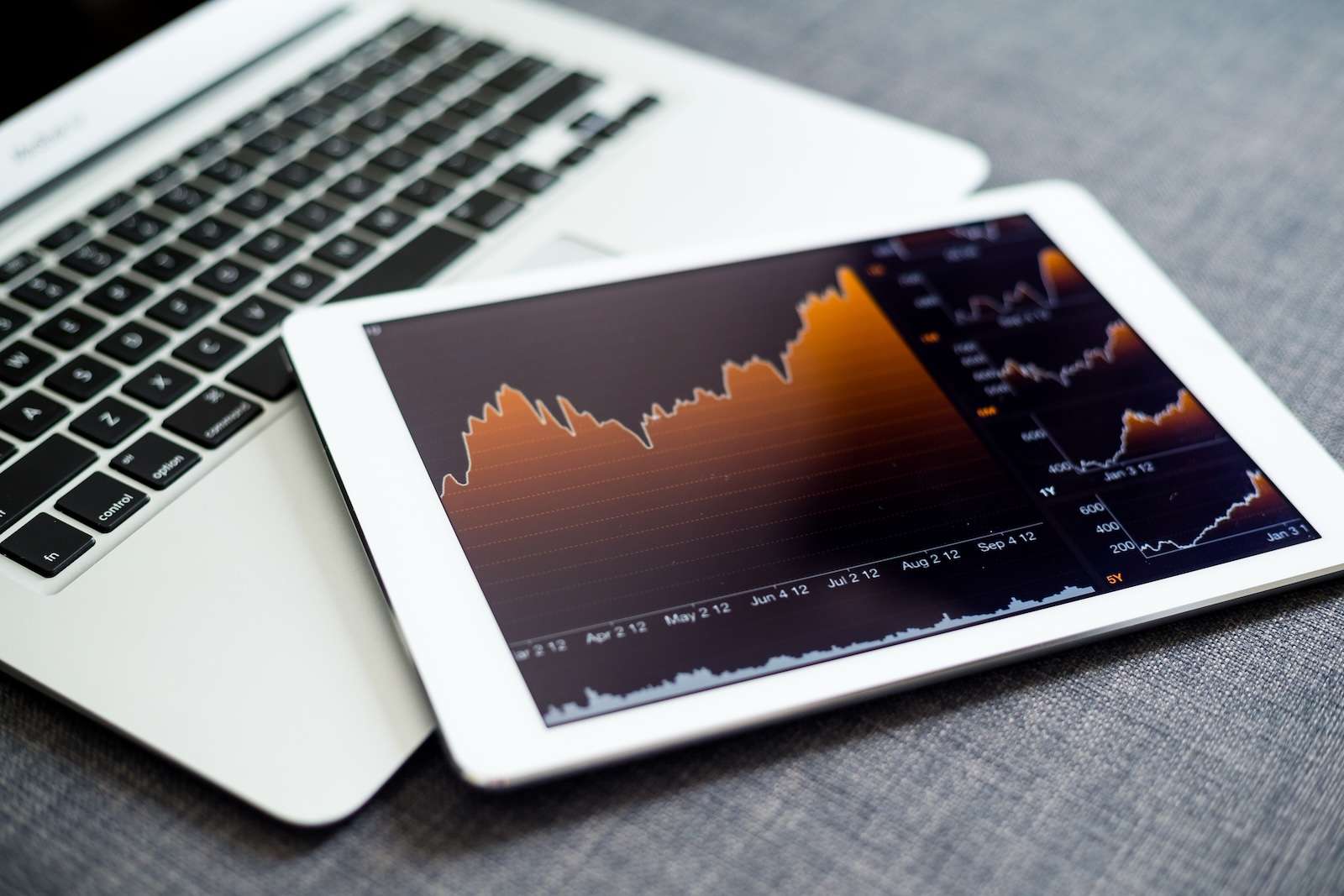 Tablet displaying financial charts and stock graphs resting on a laptop keyboard